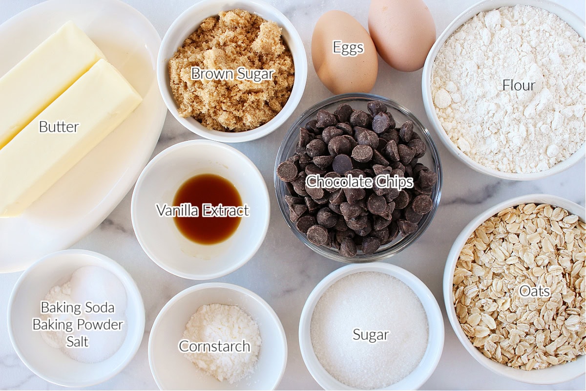 Labeled ingredients for oatmeal chocolate chip cookies on a white marble countertop.