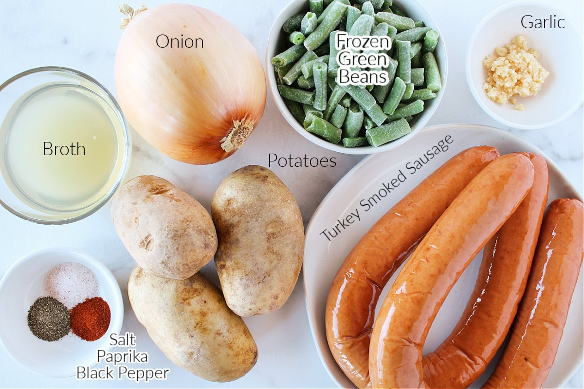 Labeled ingredients for cheesy sausage and potato bake on a white marble countertop.