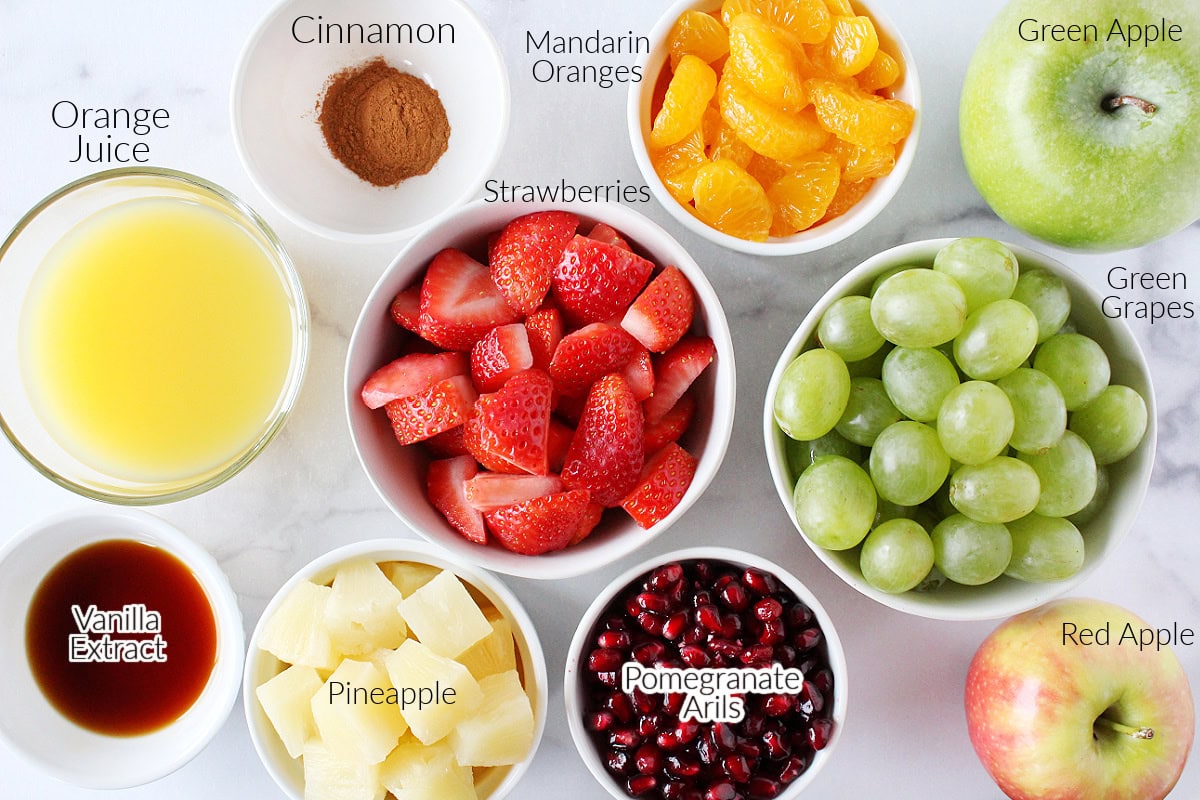 Labeled ingredients for winter fruit salad on a white marble countertop.