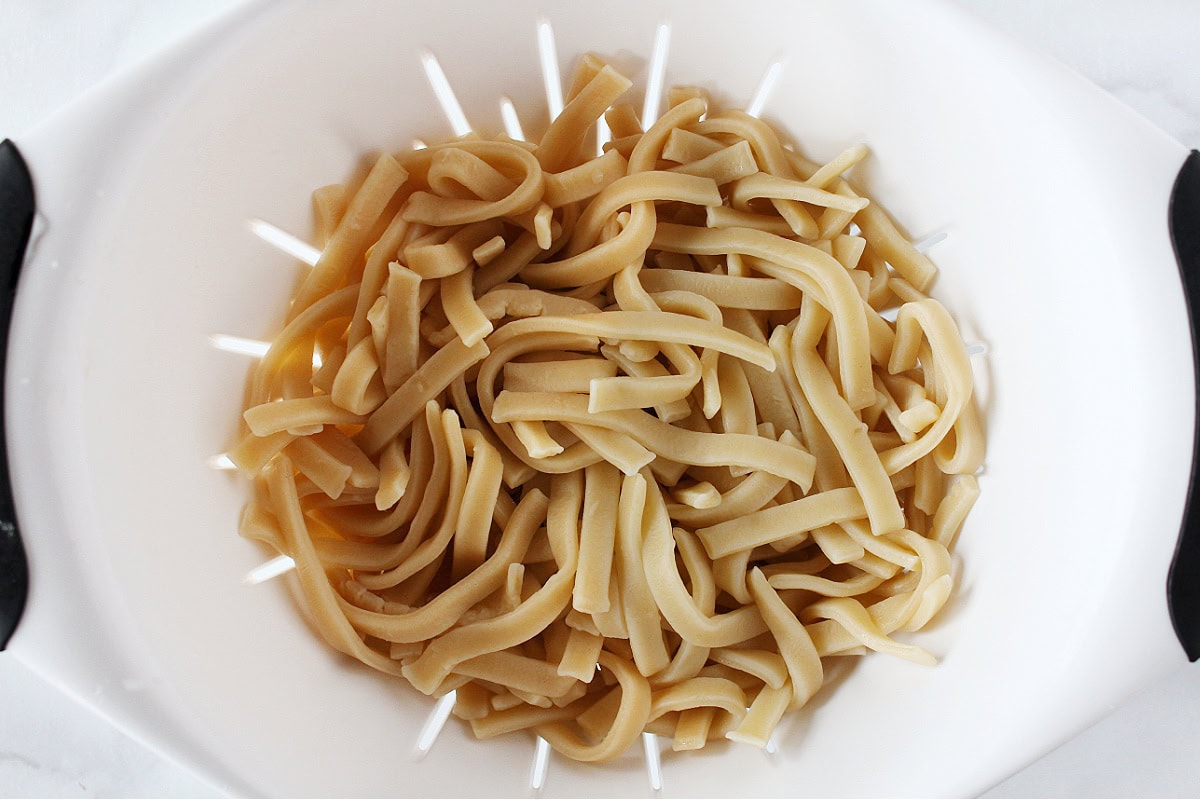 Thick pasta noodles draining in a white colander.