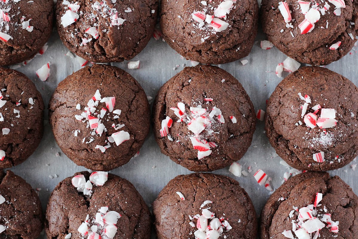 Brownie mix cookies topped with crushed candy canes on parchment paper lined baking sheet.