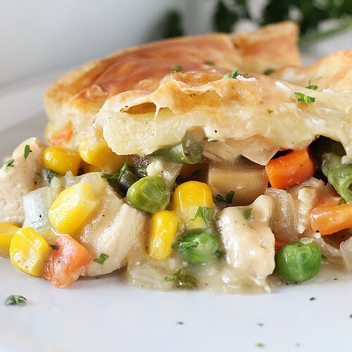 Golden puff pastry on top of veggies and chicken on a white plate.