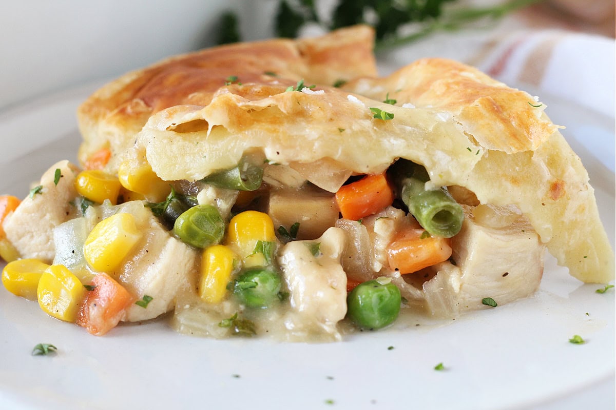 Golden puff pastry on top of veggies and chicken on a white plate.