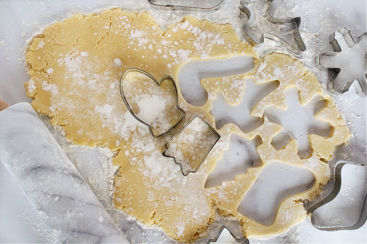 Cookie cutters in sugar cookie dough rolled out with a rolling pin.