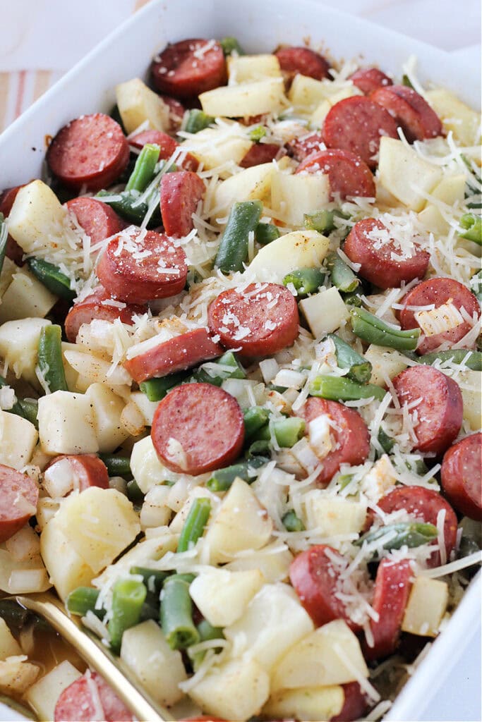 Shredded Parmesan cheese on top of baked sliced sausage and diced potatoes.