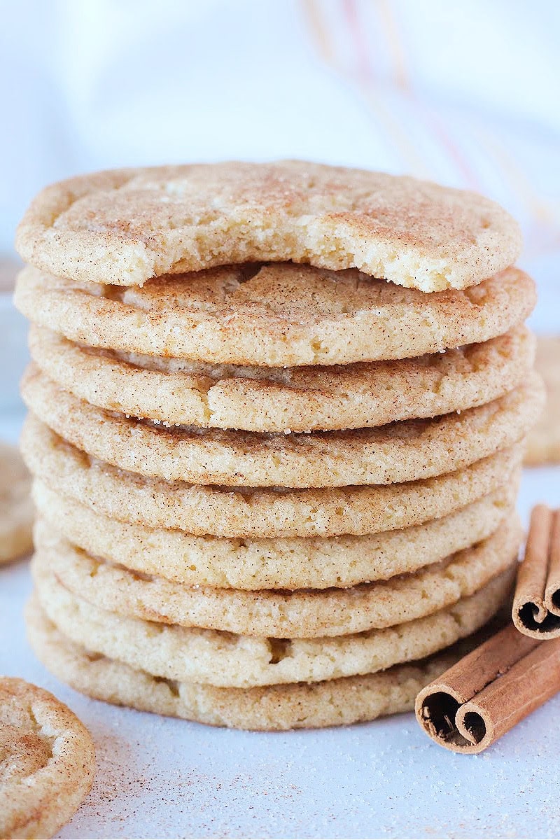 A stack of snickerdoodle cookies with cinnamon sticks beside them.