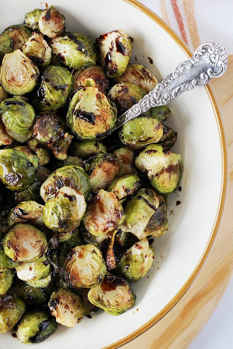 Balsamic glaze on roasted Brussel sprouts in a bowl with a vintage spoon.