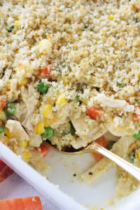 Gold spoon digging into creamy chicken noodle casserole.