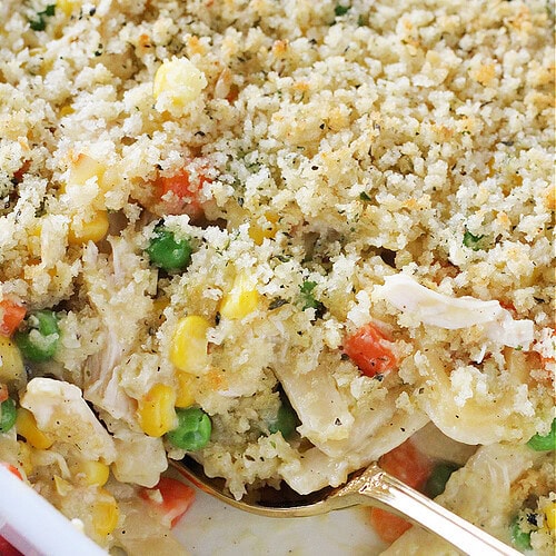 Gold spoon digging into creamy chicken noodle casserole.