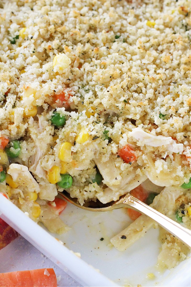 Gold spoon digging into creamy chicken noodle casserole.