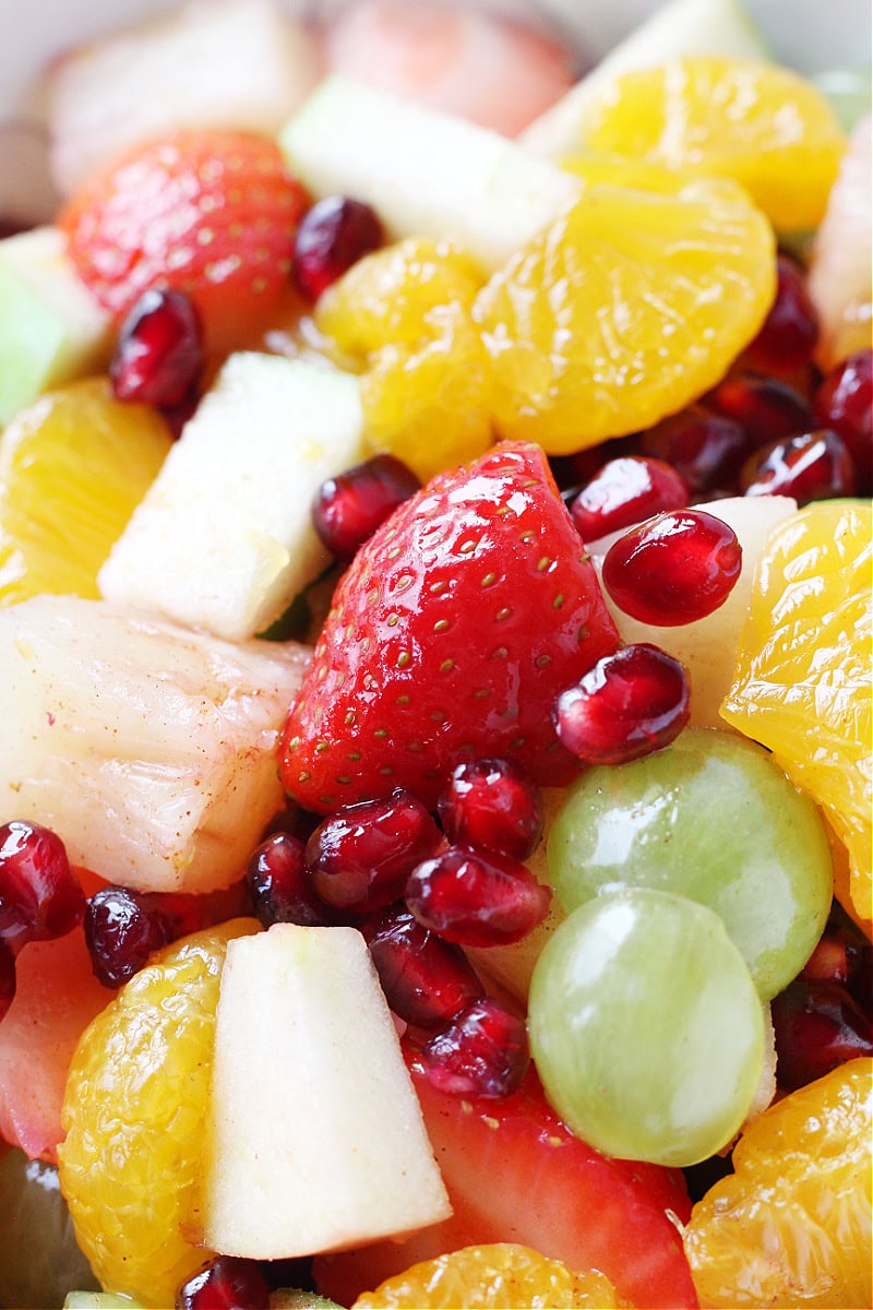 Orange cinnamon sauce covering sliced strawberries and grapes, pomegranate arils, apples, and mandarin orange slices.