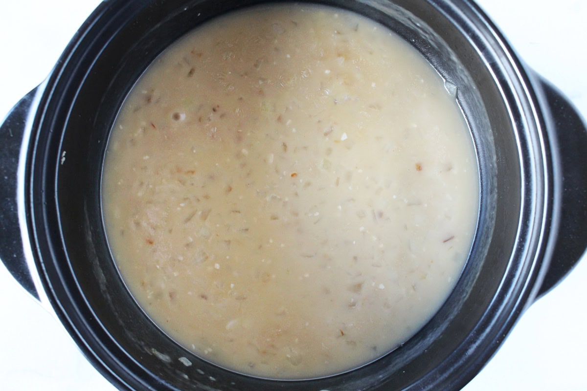 Chicken broth, onion, and garlic in a thickened sauce in a black pot.