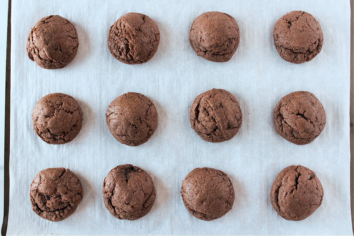 Twelve peppermint brownie cookies on a parchment paper lined baking sheet.