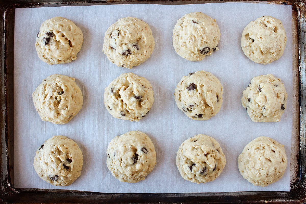 Twelve baked oatmeal chocolate chip cookies on a baking sheet lined with parchment paper.