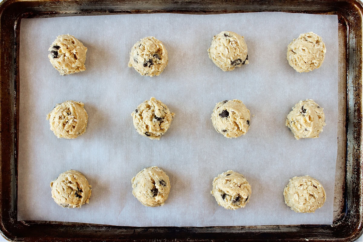 Twelve cookie dough balls on parchment paper on a baking sheet.