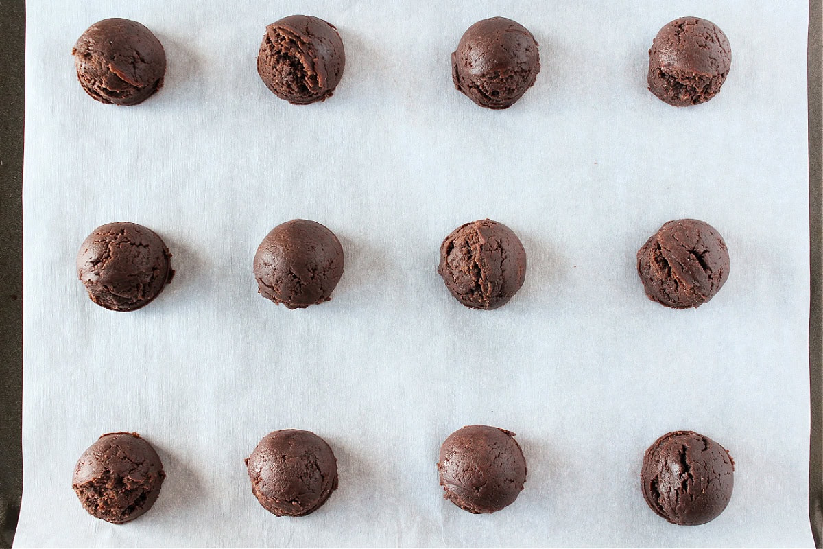 Twelve peppermint brownie cookie dough balls on a parchment paper lined baking sheet.