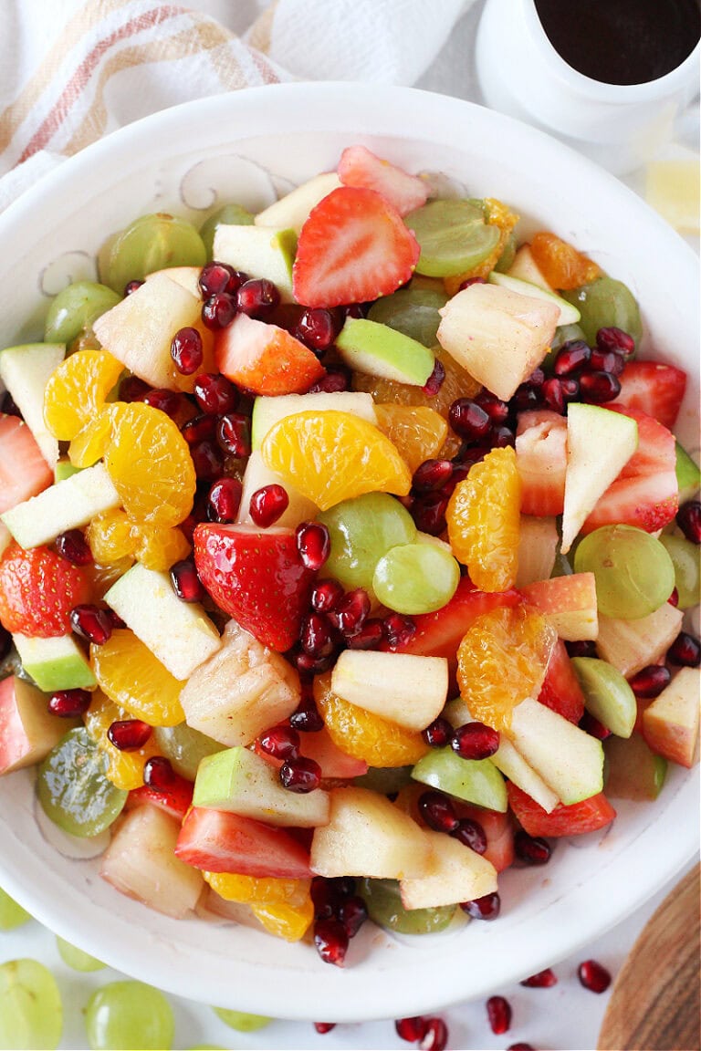 Fresh winter fruit like pomegranate arils and mandarin oranges in a white bowl.