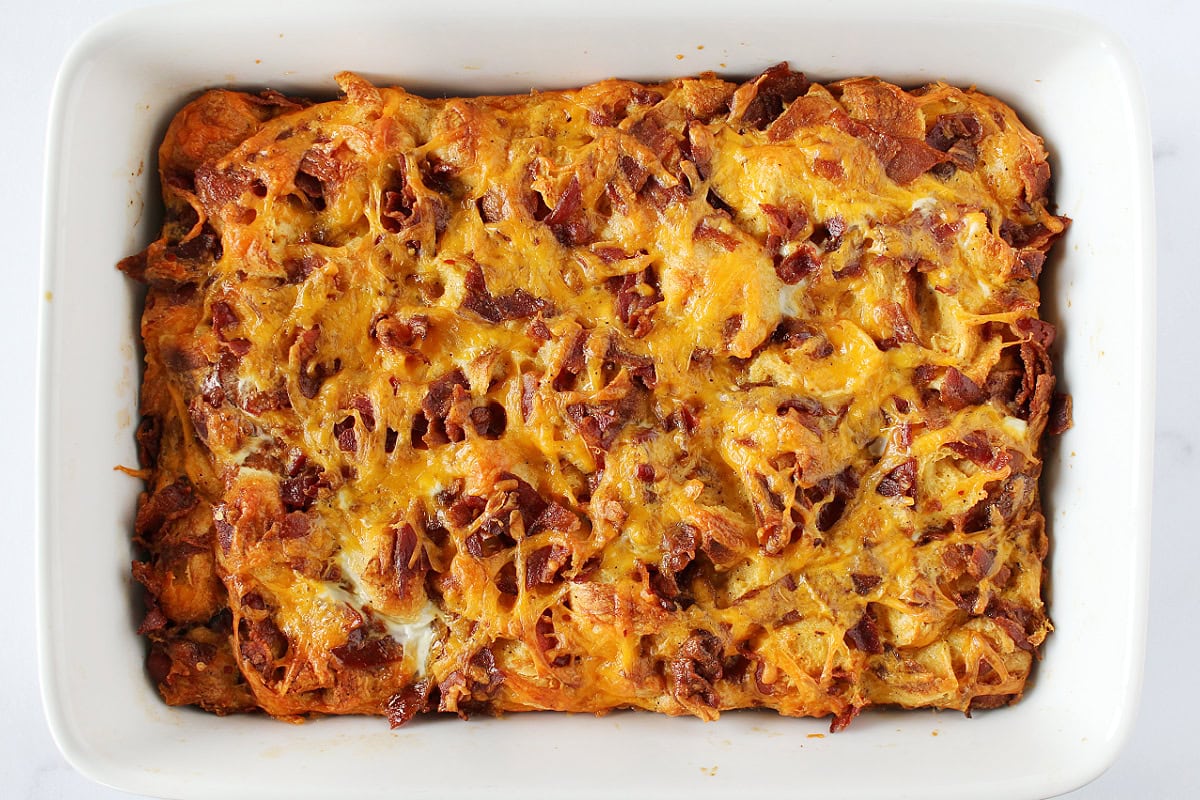 A golden brown baked croissant breakfast casserole in a white 9x13 baking dish.