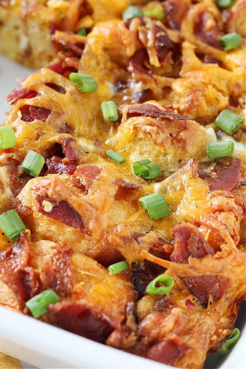 Sliced green onions on golden brown croissant breakfast casserole with bacon and cheese.