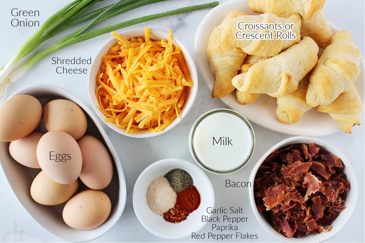 Labeled ingredients for croissant breakfast casserole on a white marble countertop.