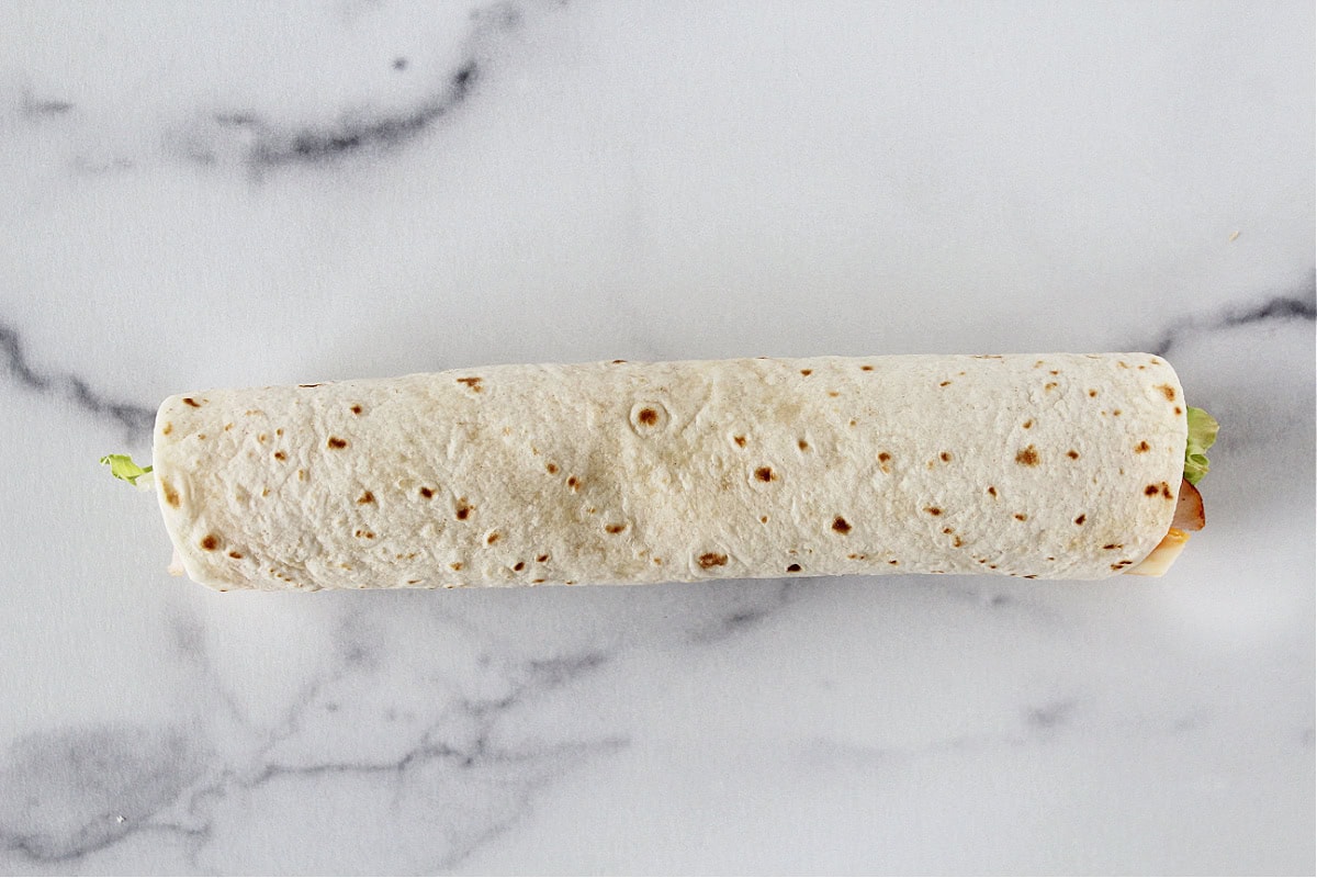 A tortilla rolled up with lunch meat, lettuce, and cheese inside.