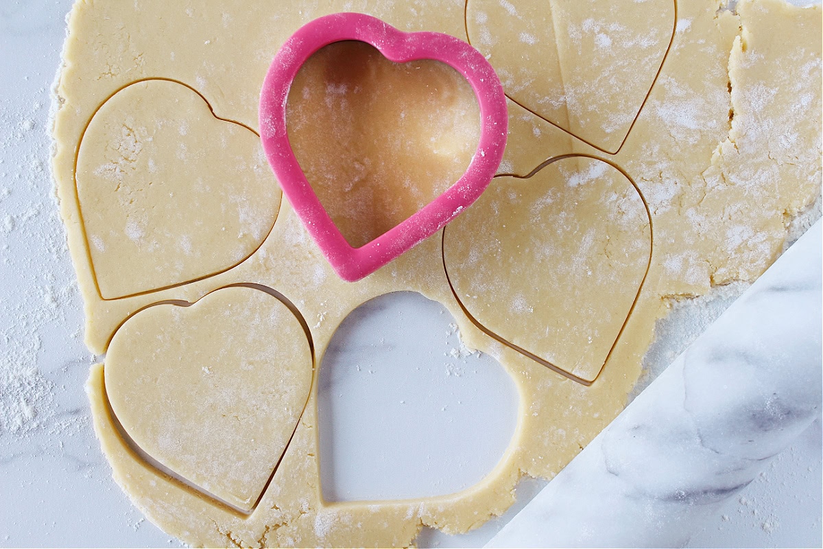 Heart cookie cutter making cookie shapes in a sugar cookie dough.
