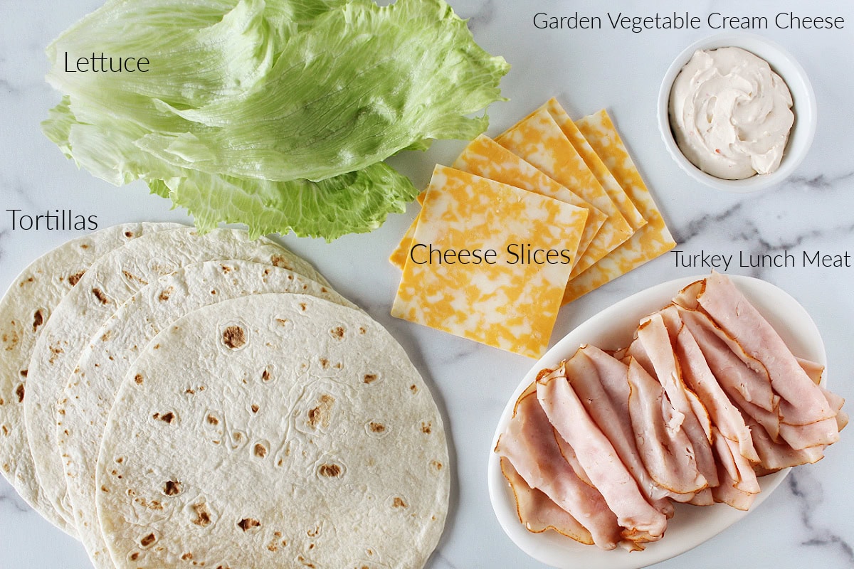 Labeled ingredients for turkey and cheese roll ups on a white marble countertop.