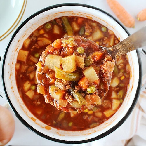 A metal ladle full of hamburger soup over the soup pot.