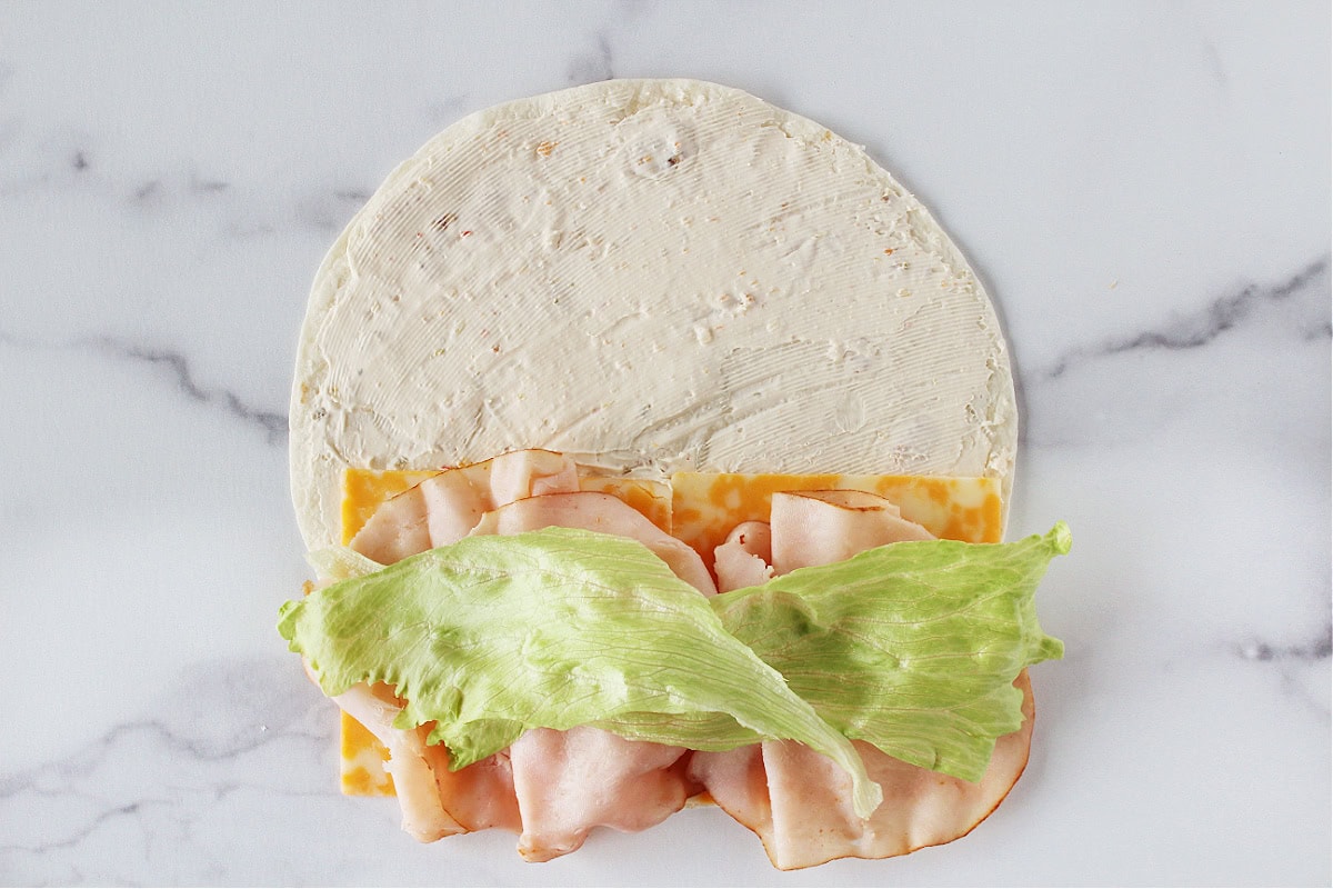 Lettuce, turkey lunch meat, and sliced cheese on a cream cheese covered tortilla.