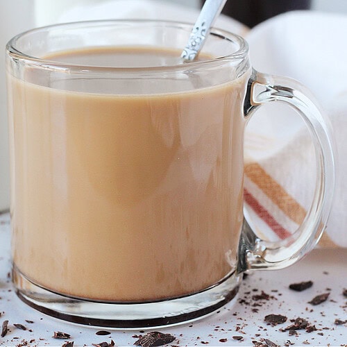 A glass mug filled with a mocha coffee and a spoon.