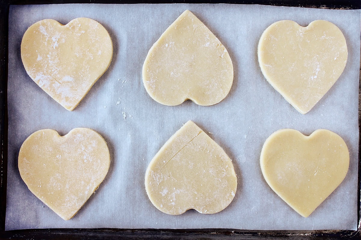 Six unbaked heart-shaped sugar cookies on a parchment paper lined baking sheet.