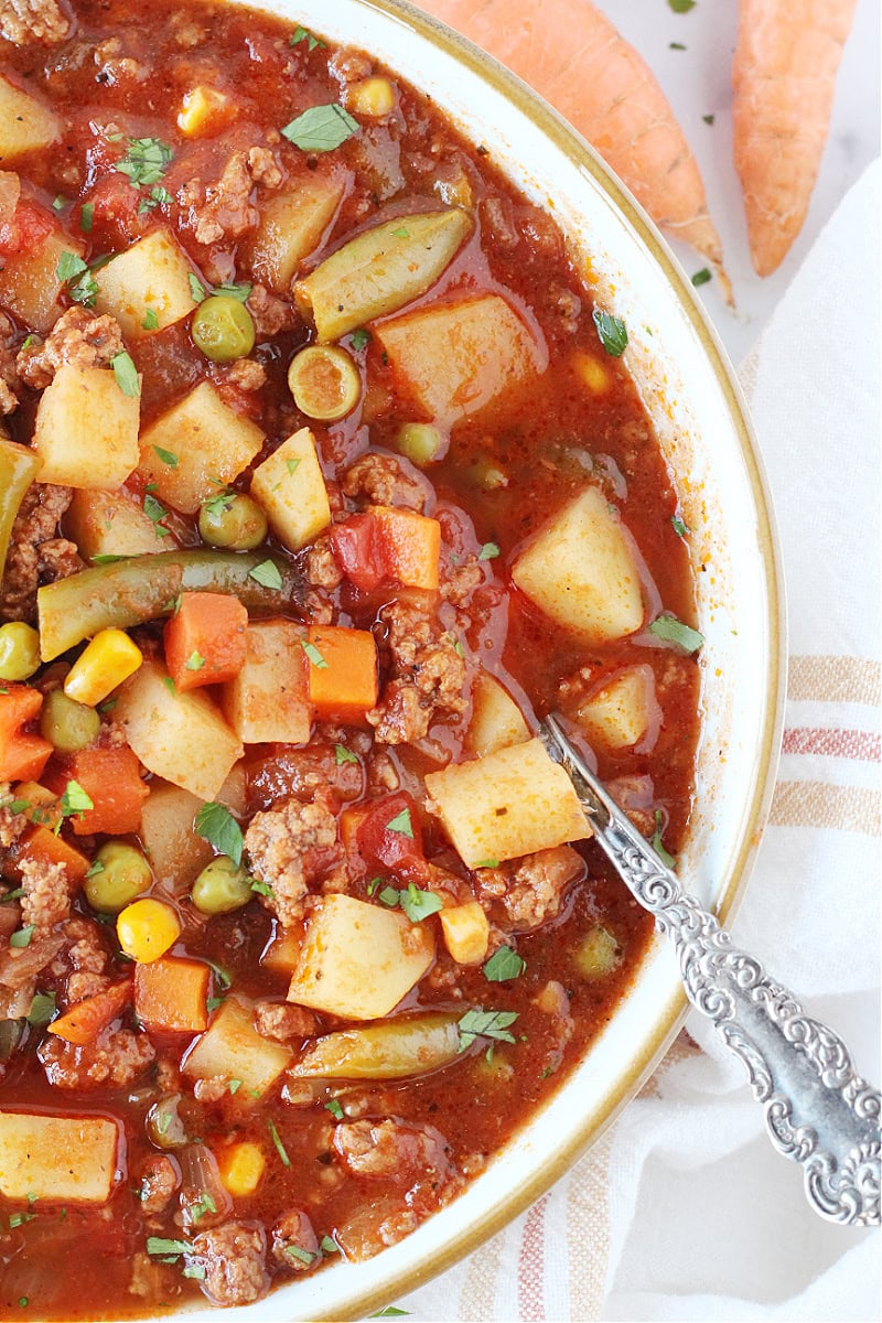 A bowl of hamburger soup in a white bowl with a vintage spoon.
