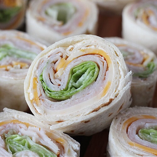 Turkey and cheese roll ups on a wooden cutting board.