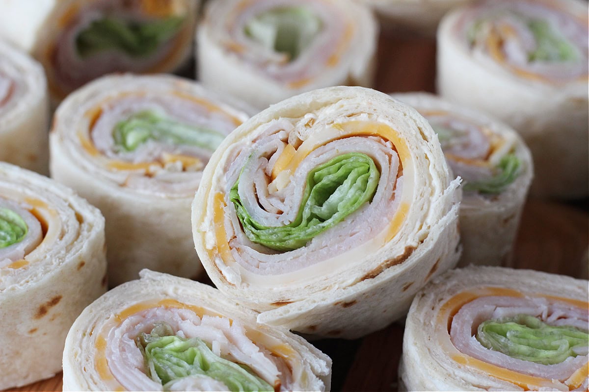 Turkey and cheese roll ups on a wooden cutting board.