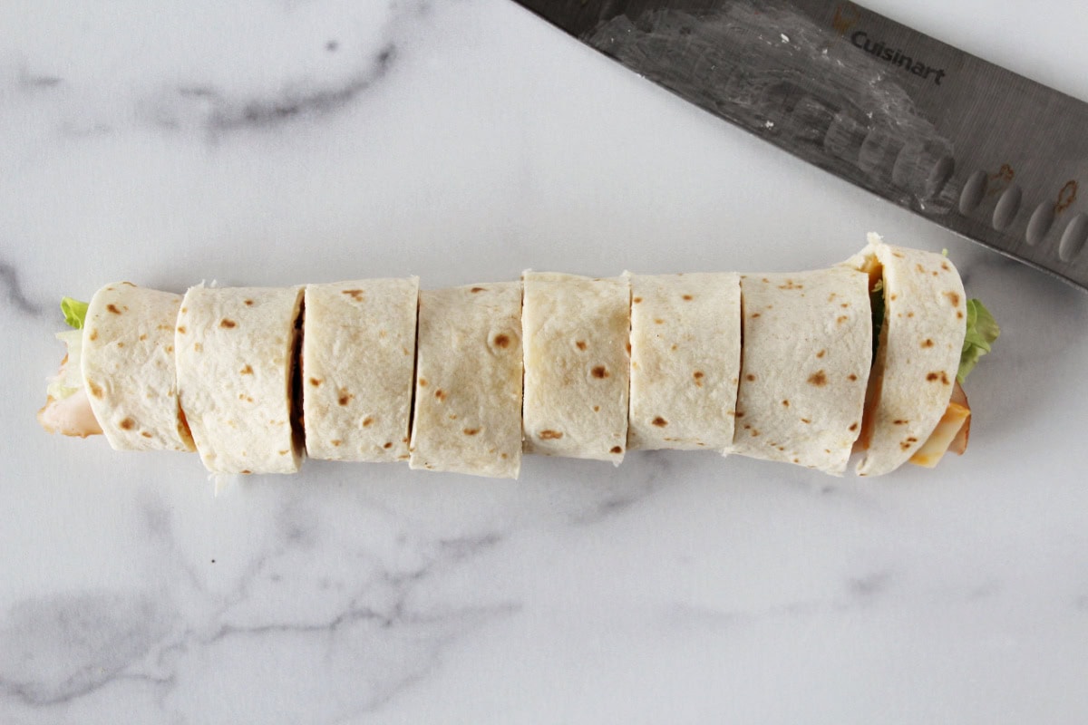 A turkey and cheese roll up cut into 8 slices on a white marble countertop.