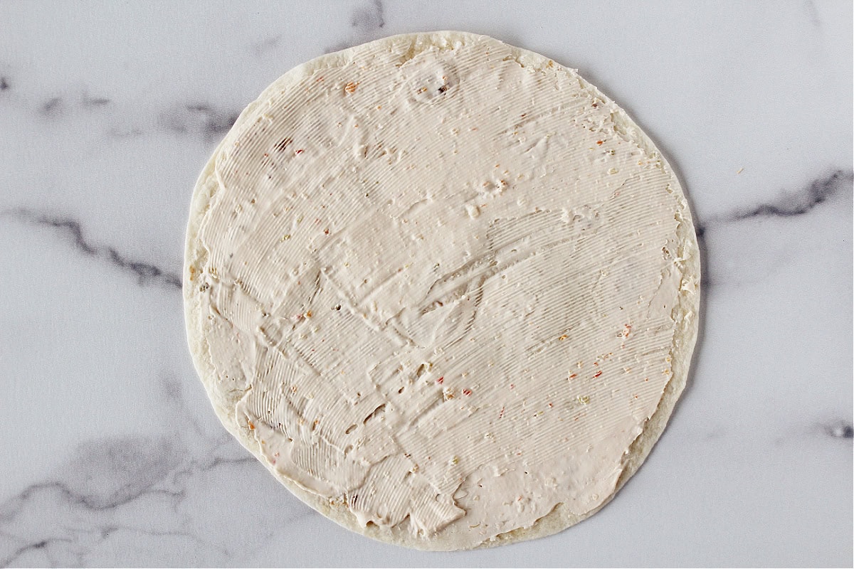 Garden vegetable cream cheese spread evenly over a tortilla.