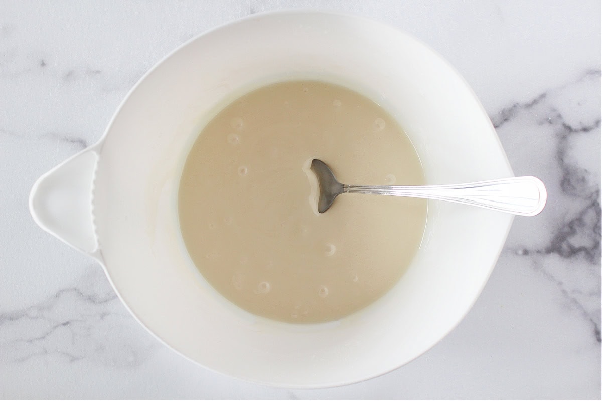 A metal spoon in a white mixing bowl with powdered sugar frosting.
