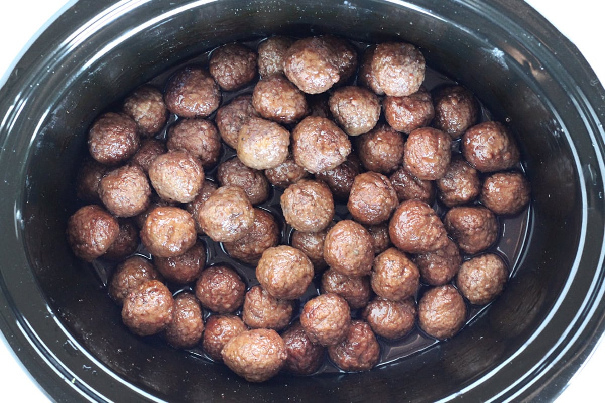 Cooked meatballs in a black slow cooker in a sauce.