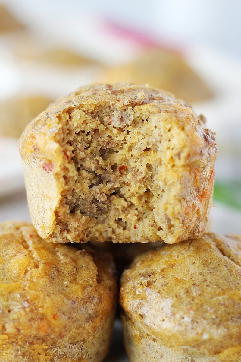 A bite taken out of a sausage pancake mix muffin stacked on more muffins.