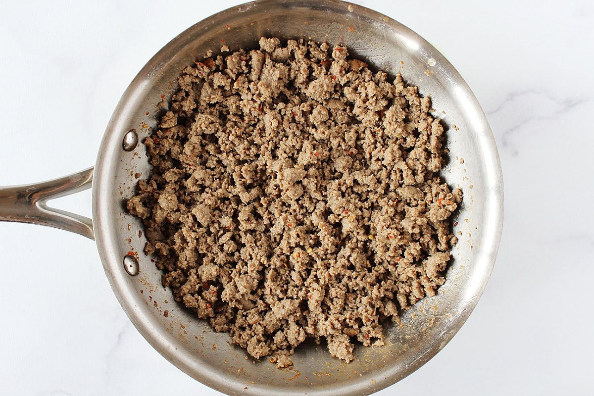 Browned ground turkey sausage with spices in stainless steel sauté pan.