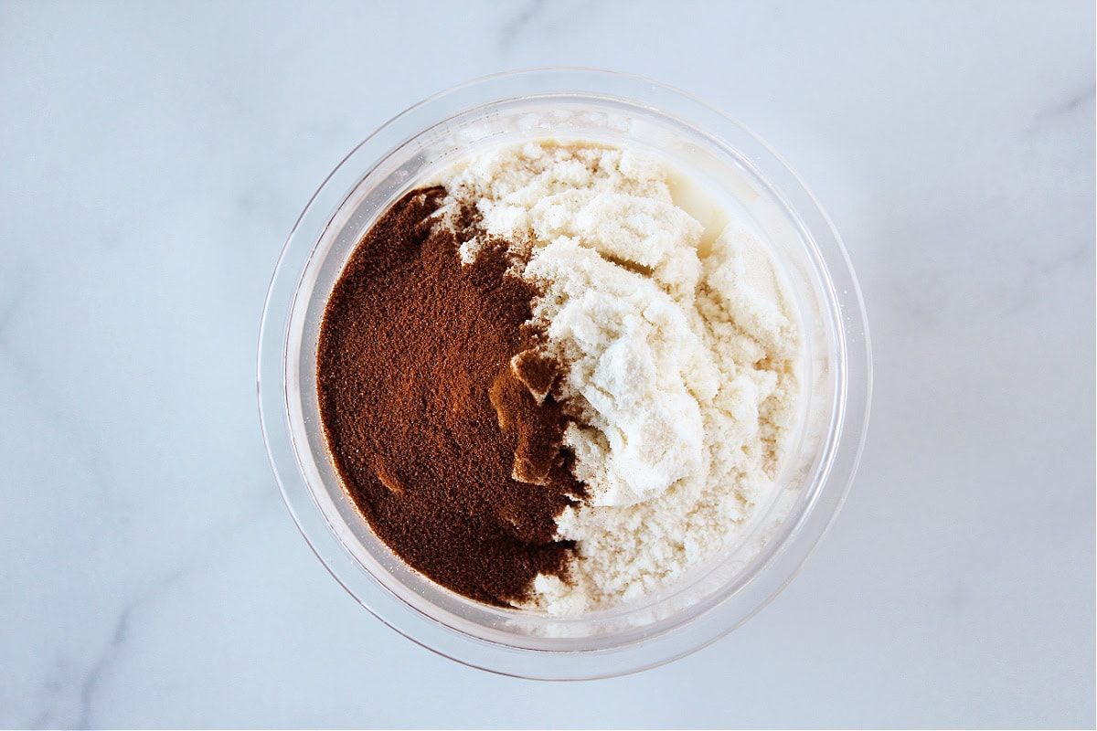 Espresso powder, and protein powder on top of milk in a plastic container.