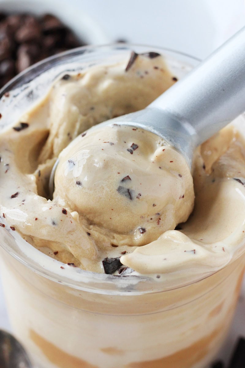 A metal ice cream scoop in a Ninja container of espresso ice cream with chocolate chunks.