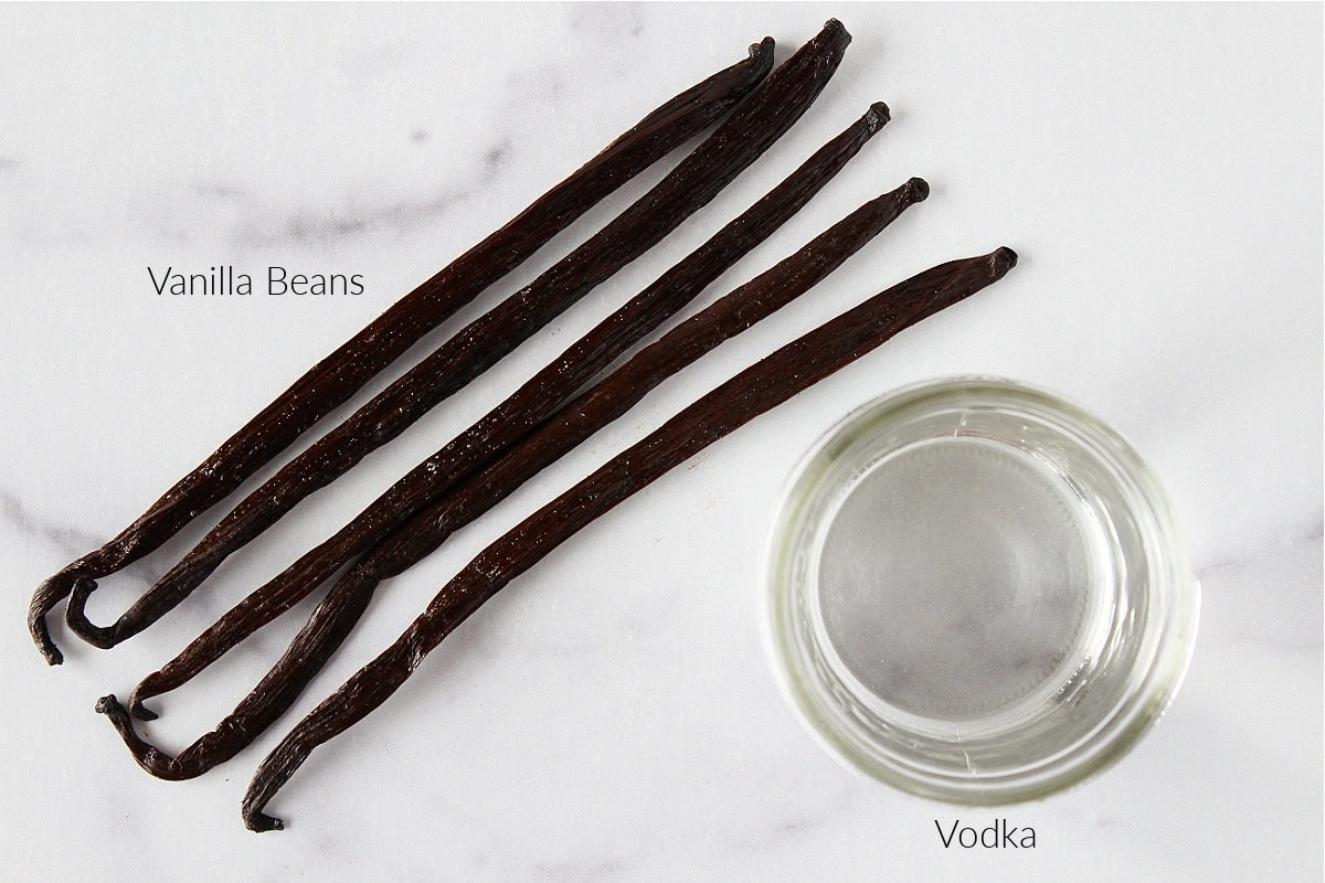 Labeled ingredients for homemade vanilla extract on a white marble countertop.