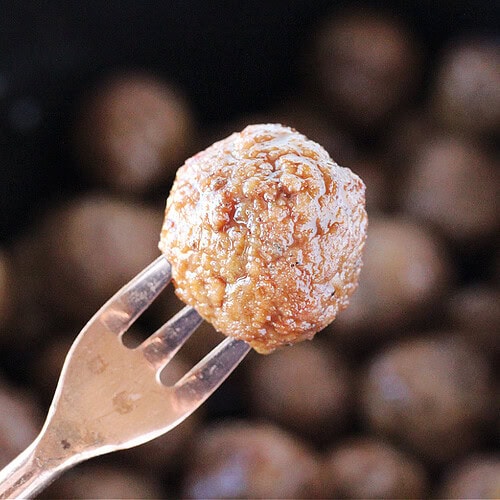 A crockpot meatball on a small copper appetizer fork.