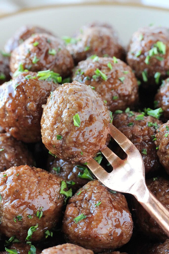 A raspberry balsamic meatball garnished with parsley on a small copper fork.