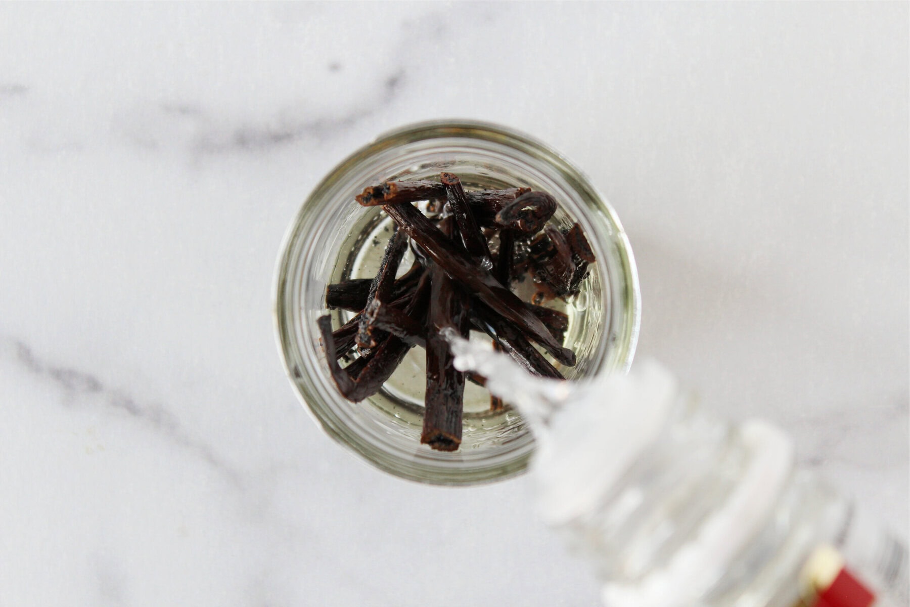 Pouring vodka in a mason jar filled with vanilla beans.