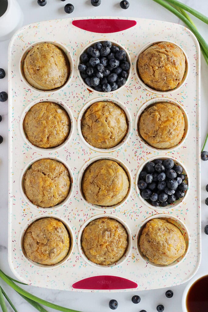 Ten sausage pancake muffins and blueberries askew in a silicone muffin pan.