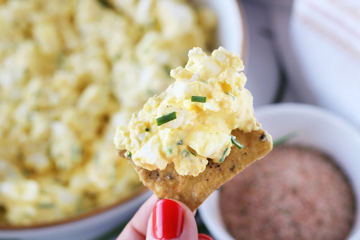 A woman's hand holding up a cracker dipped in homemade healthy egg salad.