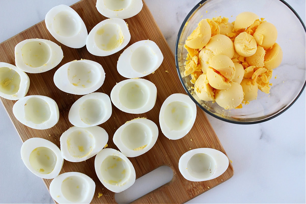 Yellow egg yolks in a bowl with the hard boiled whites on cutting board.