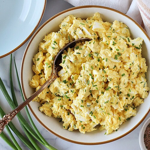 Egg salad topped with chopped chives in a white bowl with gold spoon.